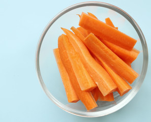 on a light blue background is a glass plate with sliced carrots. Weight loss, proper nutrition, B, C, PP vitamins, seasonal vegetables, nutrition culture. Pieces of carrots are lit by light.