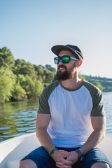 Attractive man, wearing sunglasses and a beard, enjoying a boat trip on the river in summer.