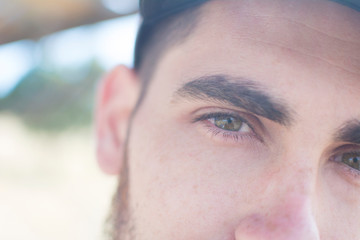 Close-up of the green eyes of a Caucasian man, with a beard and wearing a cap.