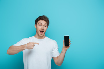 excited guy pointing with finger at smartphone with blank screen on blue background