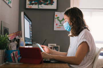 A young woman with a mask and a coronavirus positive tele-works from her home computer due to Covid-19.
