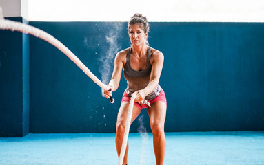 Fit woman with battle rope in training fitness gym during quarantine isolation - Person athlete...