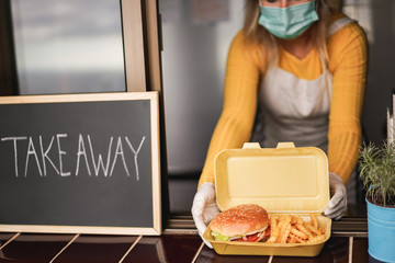 Young person preparing takeaway food inside restaurant while wearing face mask during Coronavirus...