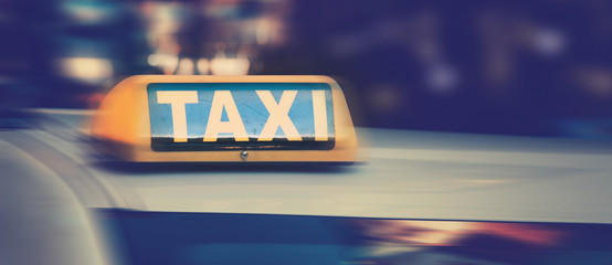 Taxi sign on top of taxi cab at night. City bokeh lights in the background. Motion blur