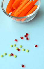 a glass plate with chopped carrot slices stands on a blue background, with red and green pills. Weight loss, proper nutrition, B, C, PP vitamins, seasonal vegetables,