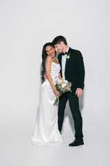 full length view of happy bridegroom hugging elegant african american bride holding wedding bouquet on white background