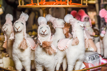 Cute alpaca stuffed toy with small hats smiling for sale in a Christmas market shop