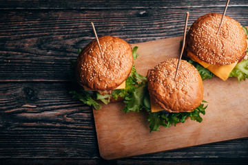 three hamburgers with meat, cheese, lettuce, tomato on a Board on a wooden table