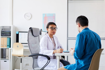 Female doctor discussing with patient his disease while sitting at the table during his visit at the hospital