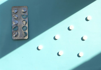 white round tablets on a light blue surface, illuminated by light. Empty packaging for pills, vitamin, dietary supplements. Health improvement, antibiotics, rise in price of medicines