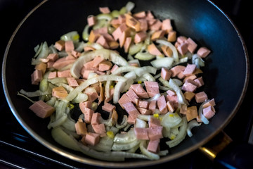 fried pieces of sausages and onion on frying pan