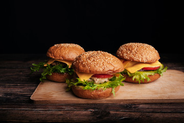 three juicy hamburgers with meat, cheese, lettuce, tomato on a wooden Board