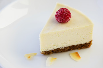 Slice of raw almond cake with raspberries and coconut on a white plate. Healthy food: lactose free, gluten free, sugar free.