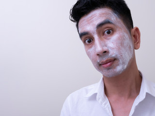 Obraz premium Asian handsome young man applying cream at his face with smiley face, Skin care concept