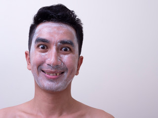 Asian handsome young man applying cream at his face with smiley face, Skin care concept