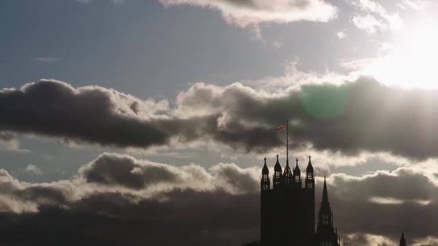 Houses of Parliament and Big Ben in Westminster silhouette against dark clouds. The union flag is flying above London