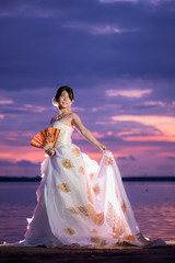 Fototapeta na wymiar バリ島の伝統風ウェディングドレス姿で夕日のビーチに立つ女性