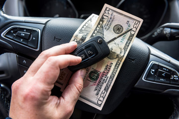 male's hand sitting in car holding dollar and car key