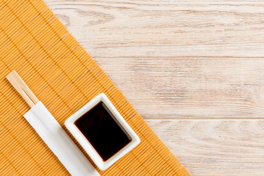 Bamboo mat and soy sauce with sushi chopsticks on wooden table. Top view with copy space background for sushi. Flat lay