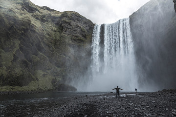 A tourist with open arms at the bottom of the Skogafoss waterfall in the golden circle of the south of Iceland