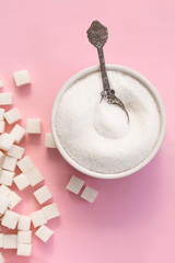 White sugar with spoon in bowl on pink background