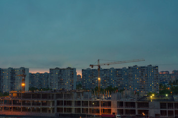 Two construction cranes over standing buildings at night. continuous infrastructure construction