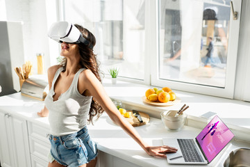 Girl in denim shorts using vr headset near laptop with online shopping website and credit card in...