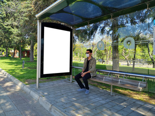 Blank white mock up of vertical light box in a bus stop. man with medical mask sitting on the bench