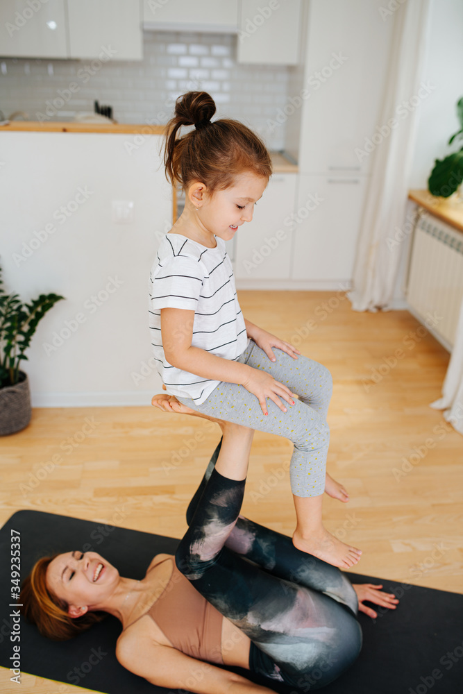 Wall mural Little girl sitting on a feet chair, doing gymnastics with her mother