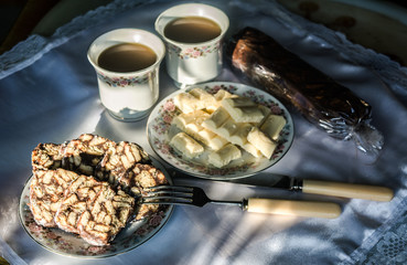 a breakfast of cookies and white chocolate with two cups of tea standing on a table on which the sun shines