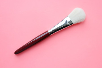 A brush made of wood, with white pile, for applying makeup, contour, powder, blush on the face, on a pink background. Beauty, fashionable female accessory brush.