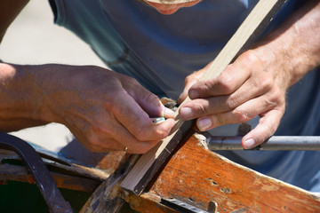Woodworker hands holding a pencil marking wooden part of boat