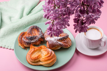 Obraz na płótnie Canvas Morning Cup of coffee with lilac flower and hot pastries. Breakfast on a pink background.