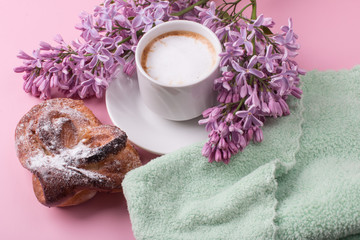 Obraz na płótnie Canvas Morning Cup of coffee with lilac flower and hot pastries. Breakfast on a pink background.