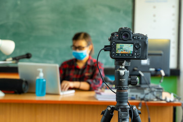 Teacher wearing protective mask to Protect Against Covid-19,Group of school kids with teacher sitting in classroom online and raising hands,Elementary school,Learning and people concept.