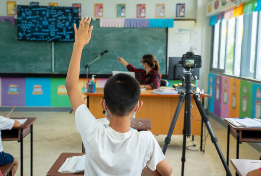 School kids wearing protective mask to Protect Against Covid-19,Group of school kids with teacher sitting in classroom online and raising hands,Elementary school,Learning and people concept. - Powered by Adobe