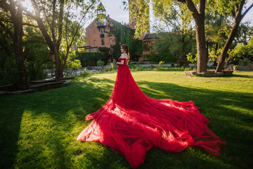 Fototapeta premium Attractive redhead woman in long red dress stays near the castle