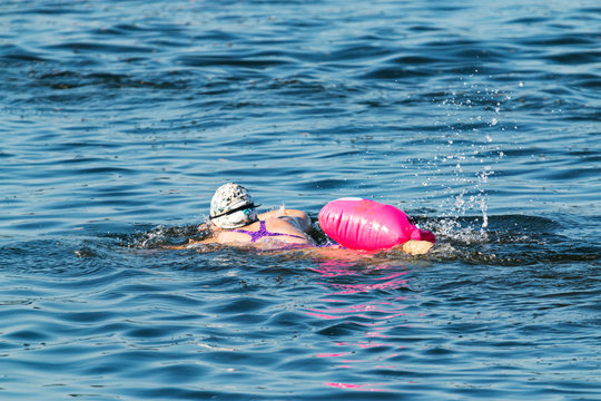 Women swimming alone with pink safety float in blue water