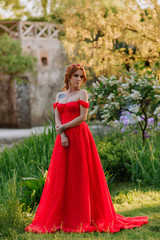 Obraz na płótnie Canvas Attractive redhead woman in long red dress stays near the castle