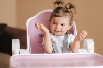 Portrait of cute baby girl sitting in high chair in the kitchen. Adorable little girl waiting for dinner