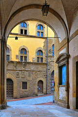 Fototapeta na wymiar TUSCANY, AREZZO. Columns and arches in old narrow street in historical centerof Arezzo with facade of medieval buildings. Italy