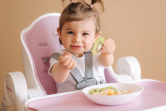 Portrait Of Happy Little Kid Eating Kiwi In High Chair. Healthy Nutrition For Kids