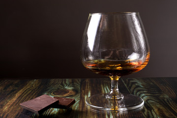 Glass with cognac and dark chocolate. Dear elite alcohol on a dark brown background. Alcoholic drinks.