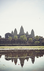 Fototapeta premium Cambodian temple monk and trees growing from the walls reflections in the water