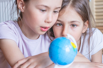 Child girl are sitting at home and looking at the globe, dreaming about traveling around the world.