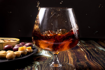 Cognac with ice sprinkled from a glass. Snack for cognac: pickled mushrooms champignons, olives and...