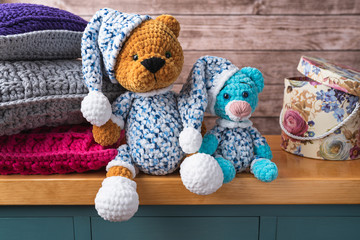 Brown and blue little bears with hats made of yarn. Plush toy sitting on a cabinet. Pillows in the background. Handiwork. Composition with free copy space for text or graphics. Teddy bear.