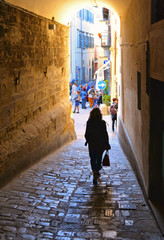 Fototapeta na wymiar Woman walks in narrow street near Corso Cavour street with people in old historic center in medieval town Citta di Castello near Perugia in Umbria, Italy