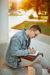 Young student studying for term exam in the park outdoors. Stylish man working at univervisty campus.
