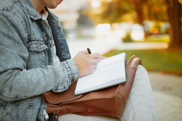 Young student studying for term exam in the park outdoors. Stylish man working at univervisty campus.